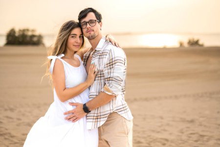 Photo for Portrait of beautiful pregnant woman and man embracing each other and looking at camera at beach - Royalty Free Image