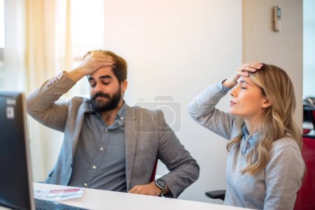 Business woman and man holding hands over forehead shocked by forgetting important meeting and realizing missing deadline for company project.