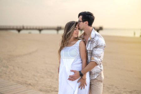 Photo for Happy embraced couple at beach. Handsome man hugging his pregnant wife and enjoying together tranquil moments at sunset - Royalty Free Image