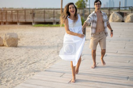 Téléchargez les photos : Beau jeune couple allant se promener sur la plage au coucher du soleil - en image libre de droit