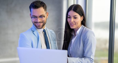 Téléchargez les photos : Deux hommes d'affaires souriants utilisant un ordinateur portable lors d'une réunion au bureau - en image libre de droit
