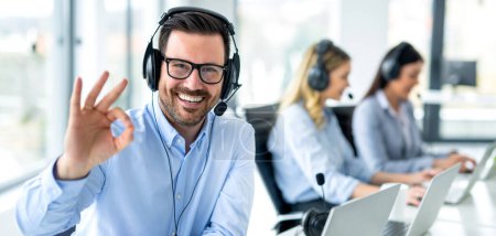 Photo for Panoramic view of handsome customer service representative showing approval sign to camera, smiling and gesturing okay at call center. - Royalty Free Image