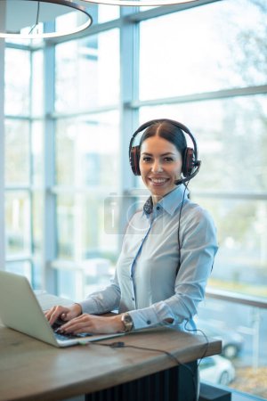 Photo for Young woman in headphones using laptop for online work - Royalty Free Image