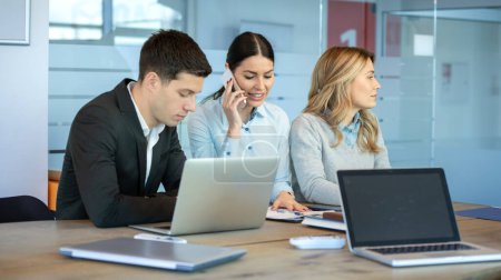 Photo for Business coworkers in smart casual wear working in office. Busy businesswoman talking on phone, handsome businessman using laptop and middle aged businesswoman looking away in contemporary workspace. - Royalty Free Image