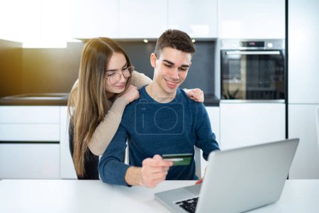 Téléchargez les photos : Jeune adolescent couple shopping en ligne avec carte de crédit et ordinateur portable à la maison - en image libre de droit