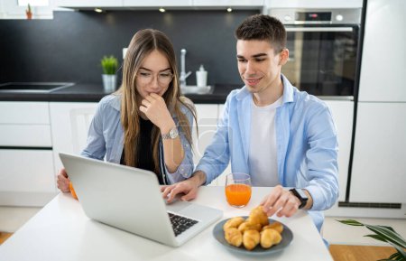 Téléchargez les photos : Adolescents femmes et hommes utilisant un ordinateur portable ensemble et mangeant des croissants - en image libre de droit
