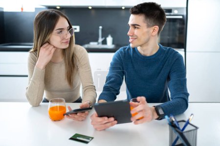 Téléchargez les photos : Beau jeune couple adolescent avec tablette et smartphone parlant et se regardant à la maison - en image libre de droit
