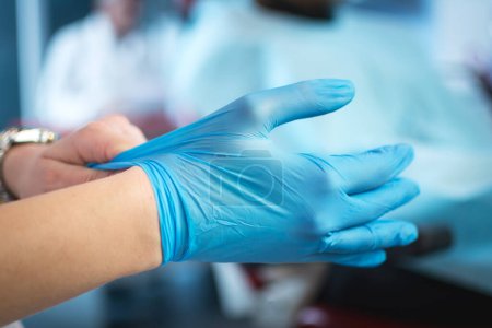 Foto de Primer plano de las manos de las médicas poniéndose guantes quirúrgicos esterilizados azules en el consultorio. - Imagen libre de derechos