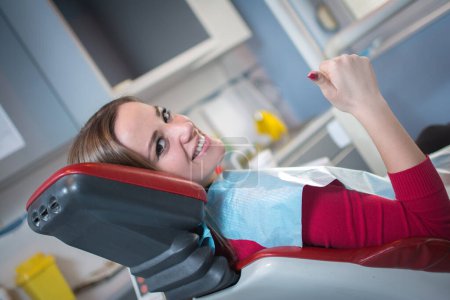 Téléchargez les photos : Portrait d'une jeune patiente adulte souriante et montrant le pouce en dentisterie. - en image libre de droit