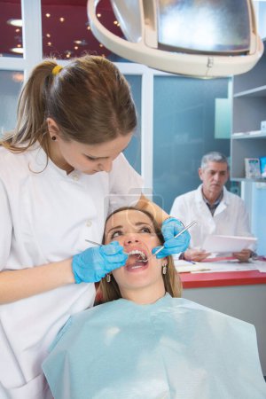 Foto de Mujer joven en examen médico en el consultorio del dentista. Dentista en el fondo. - Imagen libre de derechos