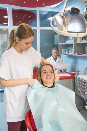Foto de Enfermera preparando a un paciente para chequeo dental. Dentista en el fondo. - Imagen libre de derechos