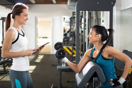 Téléchargez les photos : Entraîneur personnel féminin aidant la jeune femme sur ses routines de travail dans la salle de gym. - en image libre de droit