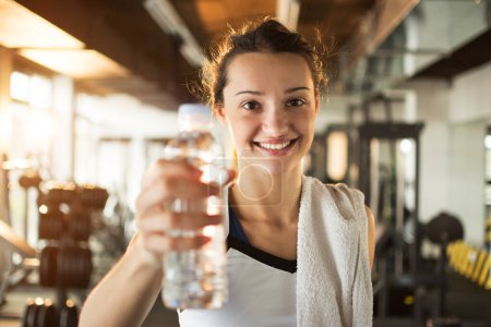 Photo for Smiling young woman holding bottle with water in gym - Royalty Free Image