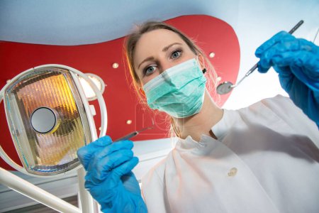 Foto de Vista de ángulo bajo del dentista femenino en máscara quirúrgica que sostiene herramientas dentales
. - Imagen libre de derechos