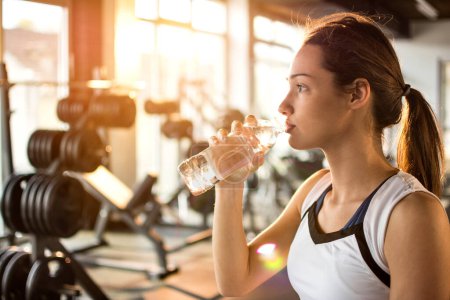 Foto de Mujer atlética joven bebiendo agua en el gimnasio - Imagen libre de derechos
