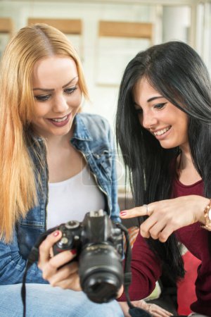 Foto de Dos jóvenes amigas sentadas y mirando fotos en cámara réflex digital. - Imagen libre de derechos