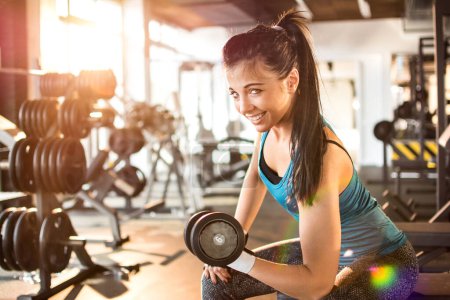 Téléchargez les photos : Jeune femme souriante soulevant haltère en acier dans la salle de gym - en image libre de droit