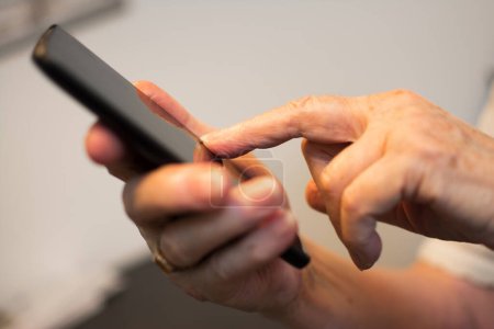 Foto de Primer plano de un dedo arrugado tocando un smartphone. - Imagen libre de derechos