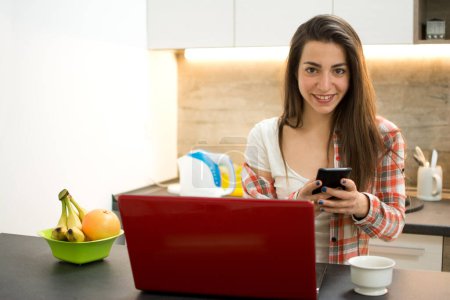 Téléchargez les photos : Belle jeune femme travaillant sur ordinateur et utilisant un smartphone. - en image libre de droit