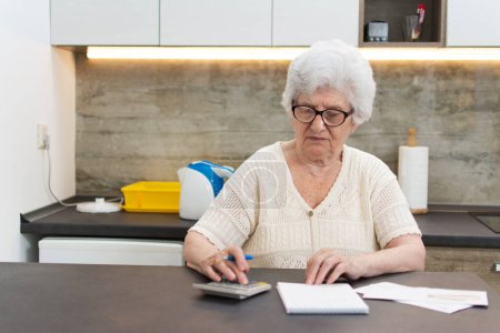 Téléchargez les photos : Femme âgée avec calculatrice et comptage des papiers à la maison. - en image libre de droit