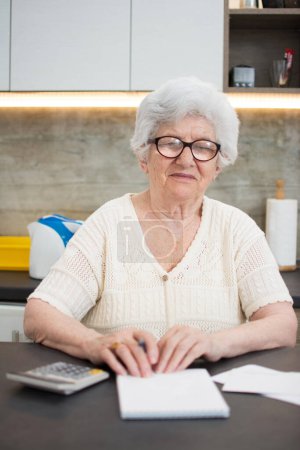Téléchargez les photos : Femme âgée avec calculatrice et comptage des papiers à la maison. - en image libre de droit