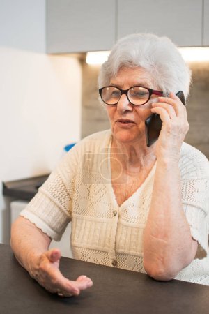 Téléchargez les photos : Heureuse femme âgée parlant sur un téléphone portable à la maison. - en image libre de droit