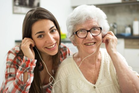 Téléchargez les photos : Petite-fille écoutant de la musique avec sa grand-mère à la maison. - en image libre de droit
