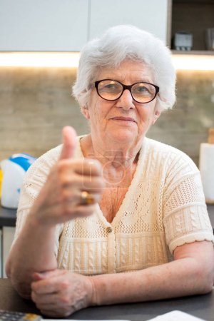 Photo for An elderly woman showing thumbs up sign at home. - Royalty Free Image