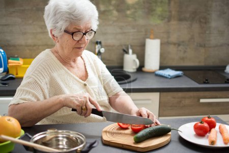 Téléchargez les photos : Femme âgée préparant des aliments sains à partir de légumes frais dans la cuisine. - en image libre de droit