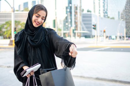 Téléchargez les photos : Belle jeune femme arabe du Moyen-Orient regardant des trucs des sacs à provisions dans la rue - en image libre de droit