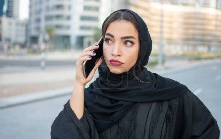 Foto de Joven mujer de negocios árabe hermosa vistiendo Abaya hablando por teléfono inteligente en la calle - Imagen libre de derechos