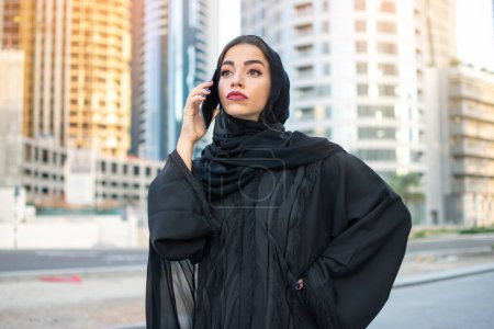 Foto de Hermosa mujer de negocios árabe vistiendo Abaya hablando por teléfono inteligente en la calle - Imagen libre de derechos