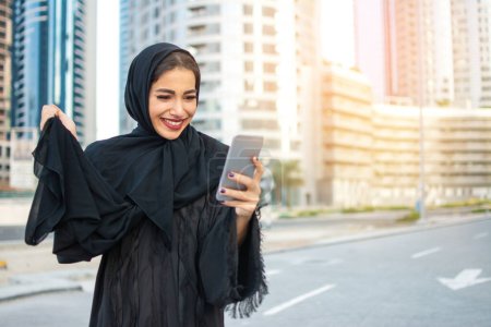 Photo for Excited muslim woman using phone on the street - Royalty Free Image