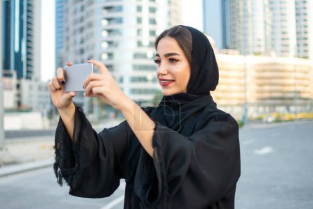 Foto de Joven hermosa musulmana mujer de Oriente Medio tomando fotos con teléfono móvil en la calle de la ciudad - Imagen libre de derechos