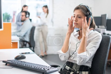 Foto de Hermosa joven agente de servicios al cliente escuchando a un cliente a través de auriculares en el centro de llamadas. - Imagen libre de derechos