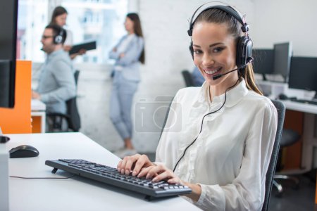 Friendly young woman working in call center office with team as the customer care operators
