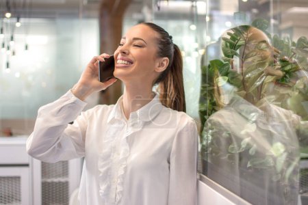 Téléchargez les photos : Joyeux jeune femme d'affaires parlant au téléphone au bureau - en image libre de droit