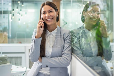 Photo for Beautiful young businesswoman talking on mobile phone in modern office - Royalty Free Image