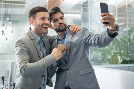 Dos guapos colegas de negocios tomando una foto selfie en la oficina