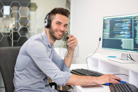 Programmation. Souriant bel homme qui travaille sur ordinateur dans une entreprise informatique, assis au bureau à écrire des codes dans le bureau.