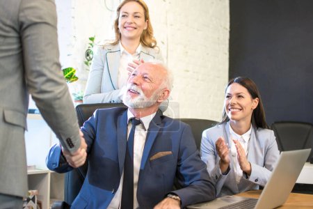 Téléchargez les photos : Homme d'affaires senior serrant la main d'un partenaire d'affaires tandis que ses collègues applaudissent au bureau - en image libre de droit