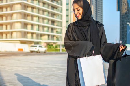 Junge Muslimin beim Einkaufen in der Stadt Abu Dhabi. Schöne arabische Frau mit Einkaufstüten auf der Straße.