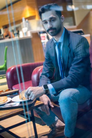 Photo for Pensive handsome businessman having lunch in cafe. Through glass window view - Royalty Free Image