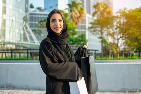 Joyeux jeune musulmane profitant du temps de magasinage dans la ville d'Abu Dhabi. Belle femme arabe avec des sacs à provisions dans la rue.