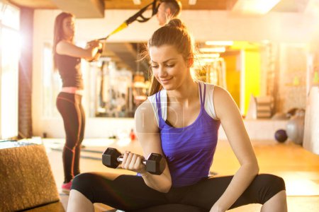 Téléchargez les photos : Jeune femme de fitness faisant des exercices avec des poids dans la salle de gym - en image libre de droit