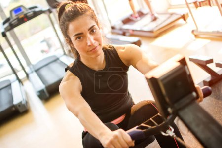 Téléchargez les photos : Jeune femme sportive faisant des exercices sur la machine de gymnase dans le centre de fitness - en image libre de droit