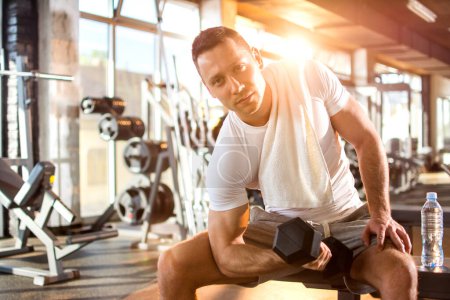 Téléchargez les photos : Jeune homme beau exercice avec un haltère dans la salle de gym - en image libre de droit