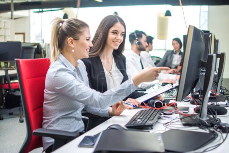 Téléchargez les photos : Deux femmes d'affaires souriantes travaillant sur ordinateur au bureau - en image libre de droit