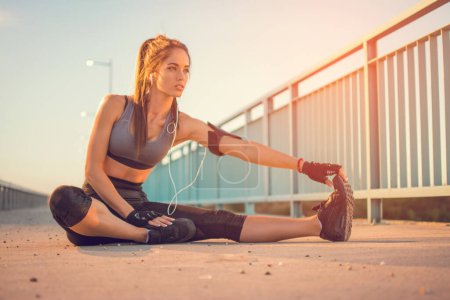 Young sportswoman stretching and touching her toes with her hand outdoors. Sporty girl stretching on the bridge