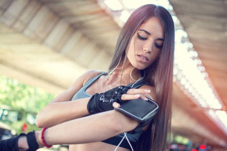 Foto de Retrato de mujer joven tocando teléfono inteligente en el brazalete al aire libre - Imagen libre de derechos